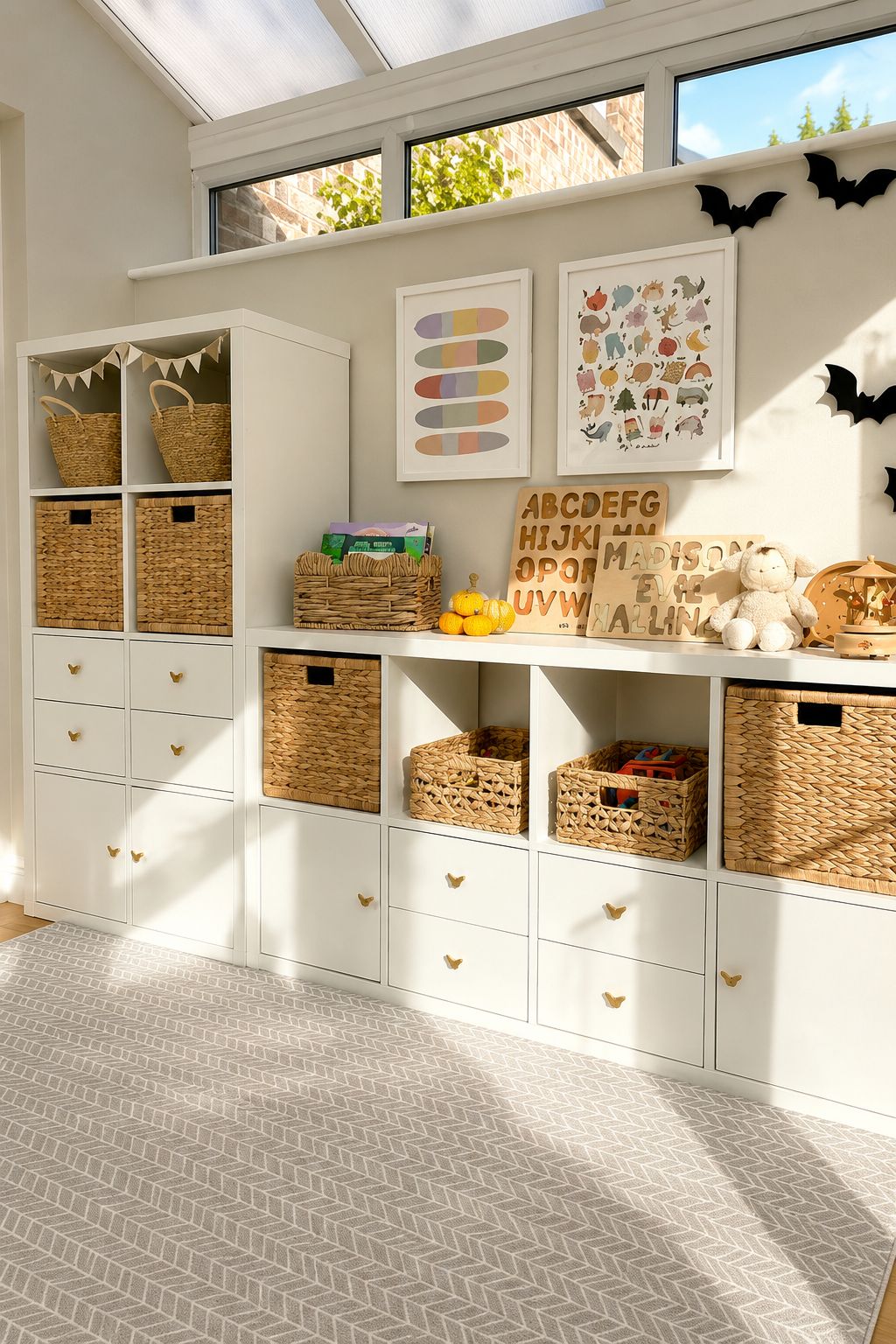 Bright neutral playroom featuring white IKEA KALLAX storage units styled with woven baskets, white drawer inserts, and children’s decor. Educational wall art, butterfly drawer knobs, wooden toys, and warm natural textures create a cozy and organized toy storage space filled with soft sunlight.